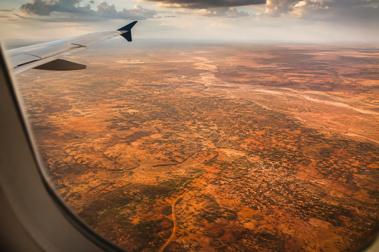 Uitzicht uit een vliegtuigraam over het uitgestrekte, roodbruine binnenland van Angola